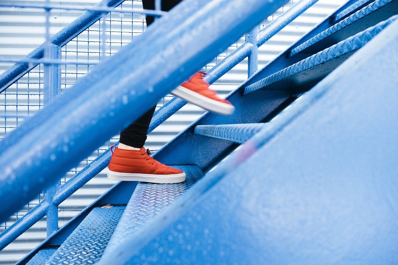 Ausschnitt einer Person mit orangenen Turnschuhen, die eine Treppe hinauf geht